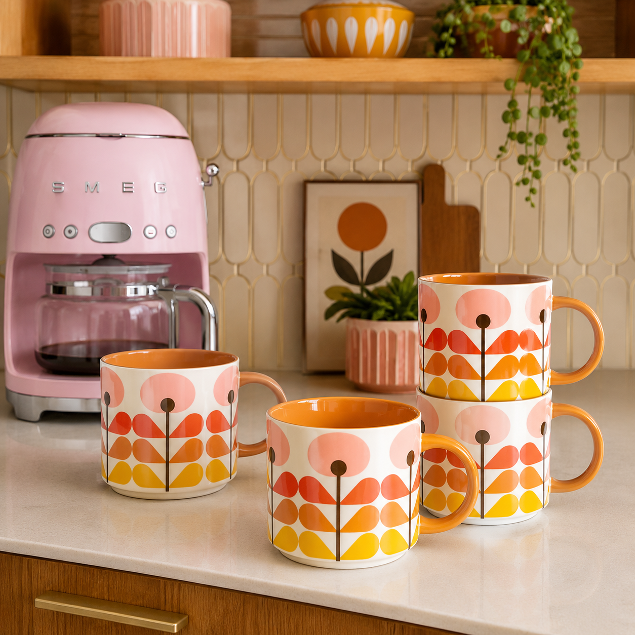 Four retro-style ceramic mugs with a floral pattern in orange, yellow, and pink on a white base, arranged on a kitchen counter next to a pink SMEG coffee machine.